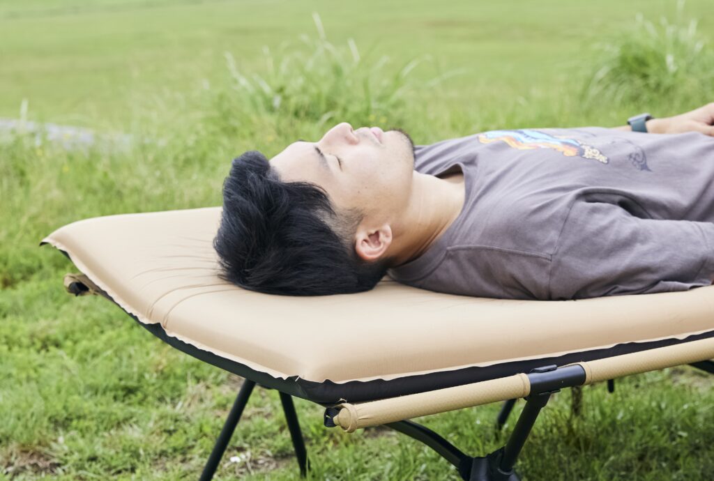 コット＆キャンプマットの上で枕なしで寝転ぶ男性