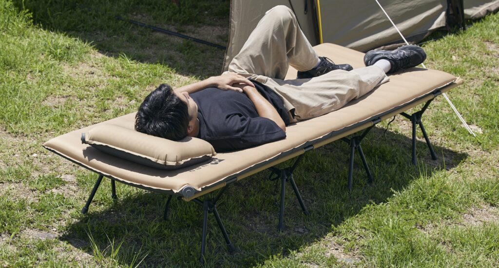コット＋キャンプマット＋キャンプ用枕を使って横になる男性